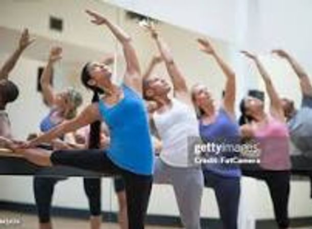 Group of women in a bright indoor fitness studio doing a ballet-inspired barre class, practicing balance and stretch exercises