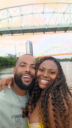Happy couple selfie on a riverfront boat with two arched bridges and city skyline at sunset