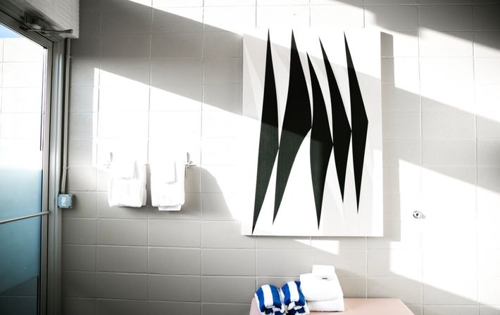 Sunlit modern tiled bathroom interior with abstract black-and-white wall art, white towels on hooks and folded blue-striped towels on a bench.