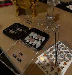 DIY Halloween nail art station with trays of embellished press-on nails, a gold skull decoration, crystal candlestick and sheets of Halloween nail decals on a tabletop.