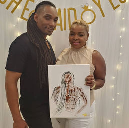 Two people smiling at an indoor celebration with string lights and a gold banner; one holds an abstract canvas painting of a long‑haired figure.