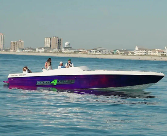 Purple speedboat with bright green "NEED 4 SPEED" decal and passengers cruising calm blue water near a sandy beachfront and low-rise coastal buildings