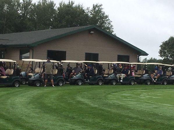 Line of golf carts with golfers waiting outside a clubhouse on a cloudy, green golf course, ready for tee time