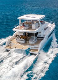 Luxury white catamaran cruising on deep blue ocean, twin-hull wake and frothy waves, rear deck lounge with sunbathers and shaded upper helm