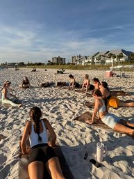 Sunlit beach yoga class: a group stretching on mats across white sand near beachfront condos under a clear blue sky