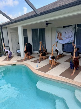 Group practicing yoga on mats along a screened backyard pool patio under a covered lanai with a decorative "Boots & Bubbly" banner