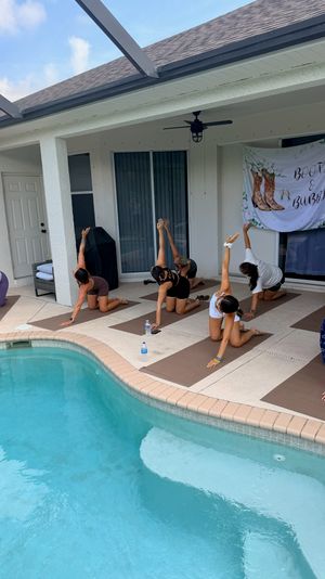 Group practicing yoga on mats along a screened backyard pool patio under a covered lanai with a decorative "Boots & Bubbly" banner