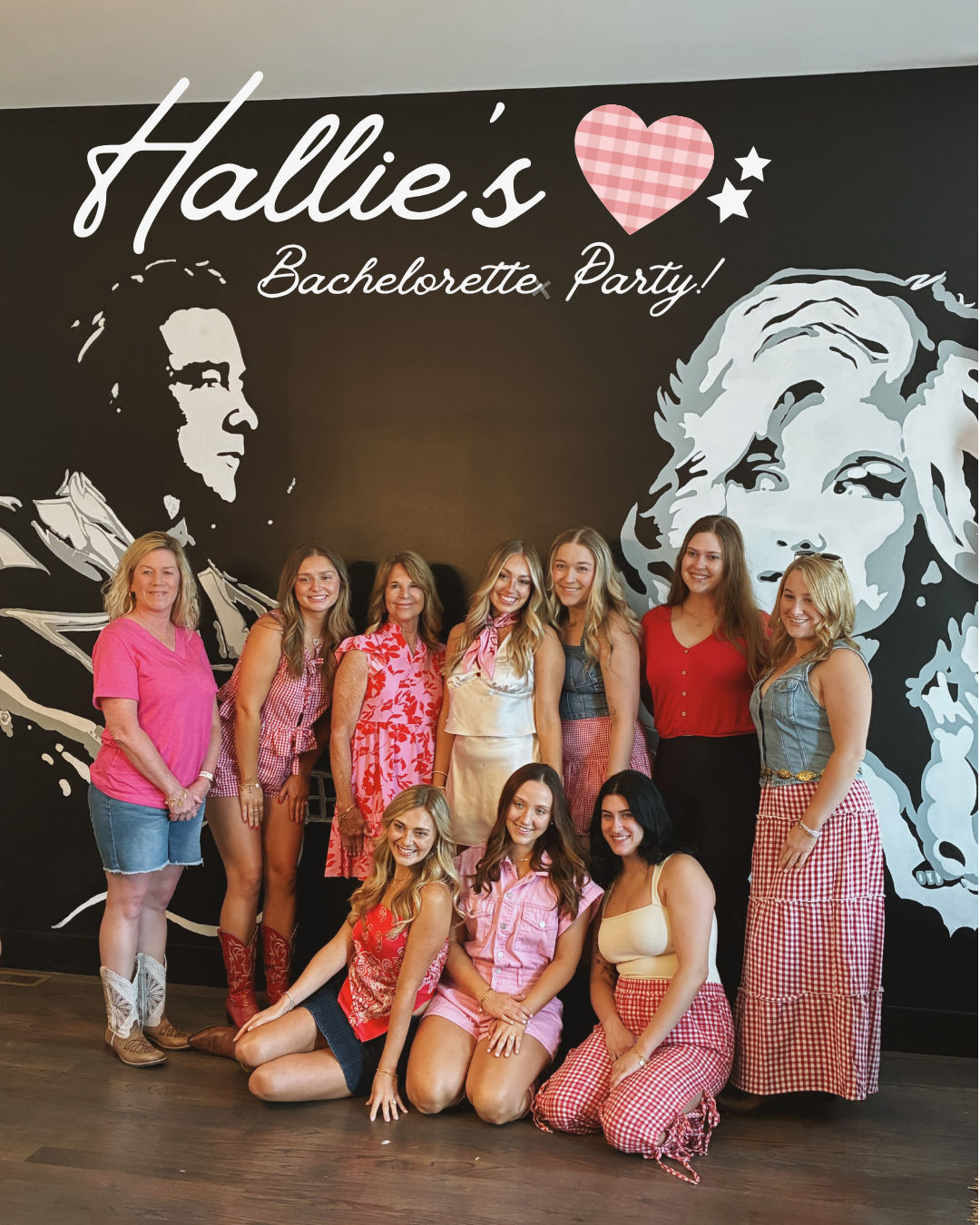 Group of ten women smiling at an indoor bachelorette party, posing in front of a large black wall mural with stylized portrait art and script signage; many wearing pink, red, gingham and denim outfits and cowboy boots.