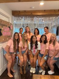 Group of women in matching pink bachelorette T-shirts and denim shorts posing indoors at a playful “Last Rodeo” themed party with cowboy boots, sneakers, silver fringe backdrop and a sign reading “Logan’s Last Rodeo, Nashville, TN”.