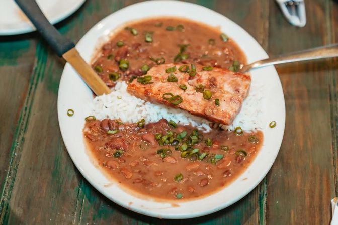 Southern-style plate of red beans and rice topped with a seared fish fillet and chopped scallions on a rustic wooden table