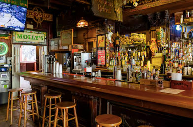 Cozy rustic pub interior with a long polished wooden bar, empty stools, crowded back bar of liquor bottles and beer taps, neon signs and a wall-mounted TV