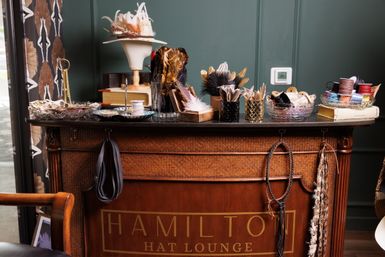 Millinery counter in a cozy hat shop displaying feather trims, ribbons, spools and a hat form on a vintage wooden desk