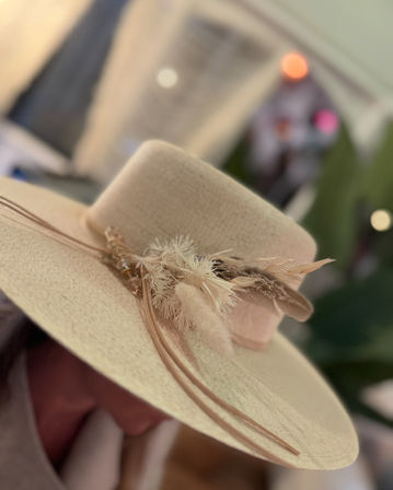Close-up of a beige wide-brim straw hat with a leather band and dried floral and feather accents — boho-chic summer accessory in neutral tones.