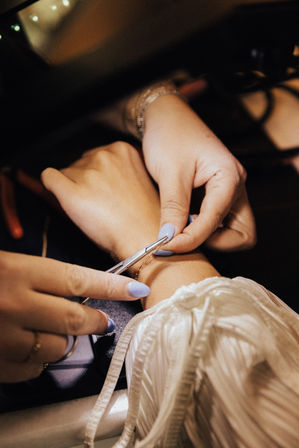 Close-up of hands with pastel blue nails using pliers to adjust a delicate gold bracelet on a wrist, jewelry repair and detailing