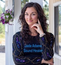 Portrait of a smiling woman with curly dark hair and a septum ring on a sunny porch beside hanging purple petunias, wearing a beaded boho jacket and bracelets.