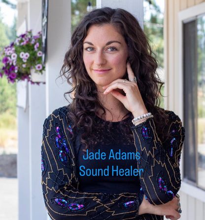 Portrait of a smiling woman with curly dark hair and a septum ring on a sunny porch beside hanging purple petunias, wearing a beaded boho jacket and bracelets.