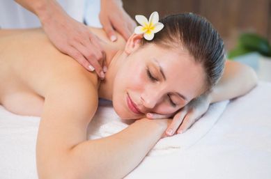 Woman with a plumeria in her hair lying on a white towel receiving a relaxing shoulder massage at a spa