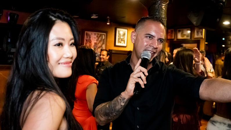 Smiling woman and tattooed man holding a microphone leading a lively karaoke night in a crowded bar interior