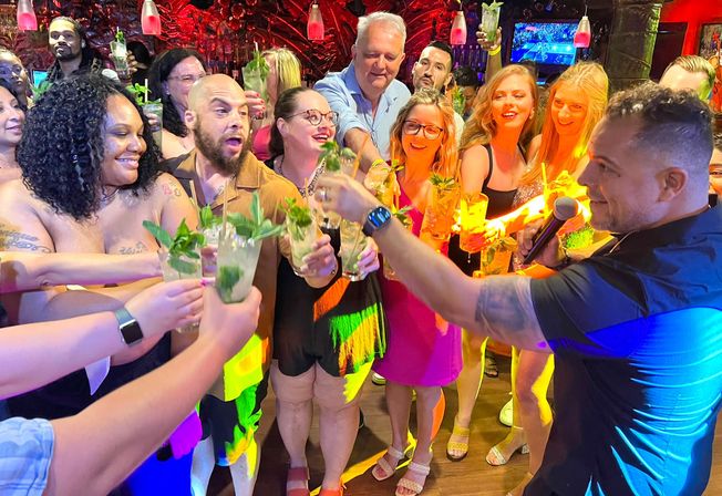 Lively nightclub scene of a diverse group raising mojito cocktails in a colorful bar while a bartender with a microphone leads a cheerful toast