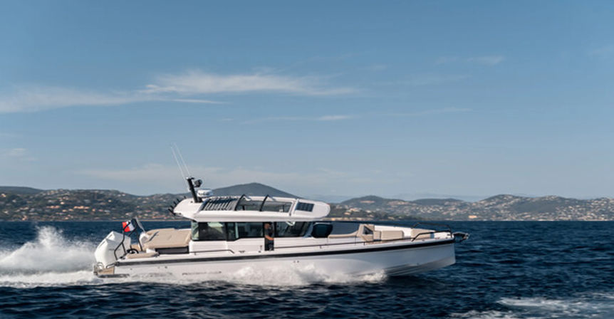 Sleek white motorboat cruising across deep blue sea with spray, hilly coastline in the distance under a clear blue sky