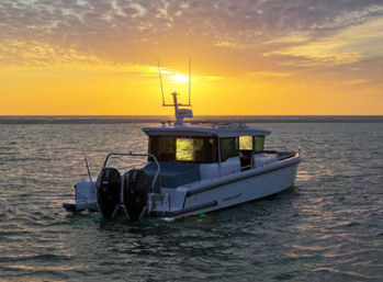 Modern cabin motorboat with twin outboard engines anchored on calm ocean waters at a golden sunset, sun glowing behind the cabin and warm reflections rippling across the sea.