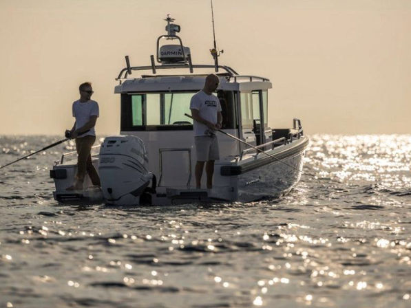 Two anglers fishing from the stern of a compact cabin boat on shimmering open water at golden hour, sunlight sparkling across the sea.