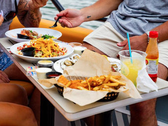 Onboard casual boat meal with basket of fries and fried fish, oysters on the half shell, nacho-topped salads, dipping sauces and a cold lemonade over the water