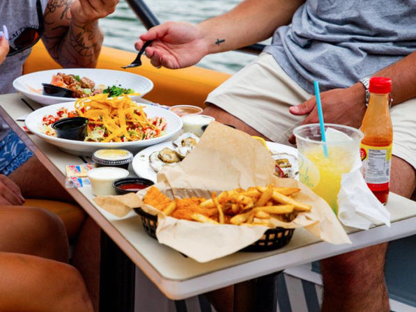 Onboard casual boat meal with basket of fries and fried fish, oysters on the half shell, nacho-topped salads, dipping sauces and a cold lemonade over the water