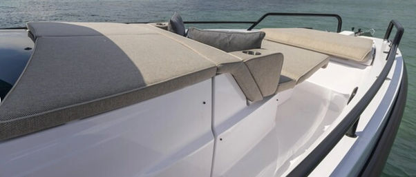 White motorboat bow with beige sun‑pad cushions and built‑in cup holder, black safety rails, floating on calm green‑blue coastal water