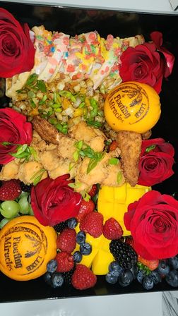 Colorful brunch box: crispy fried chicken bites, mini cereal‑topped waffle slices with icing, seasoned diced potatoes with scallions, fresh mango cubes, mixed berries and grapes, stamped oranges and red roses.