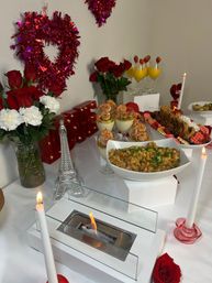 Valentine's Day brunch spread with red roses, heart tinsel decorations and candles, Eiffel Tower ornament, shrimp cocktail glasses, strawberry mimosas, bowl of savory hash, fried chicken with red waffles, and a tabletop flame feature.