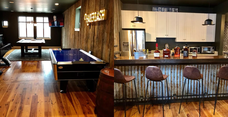 Rustic basement game room featuring an air hockey table and pool table on warm wood floors, an industrial corrugated-metal home bar with leather barstools, pendant lights, stainless fridge and bottles on the counter.