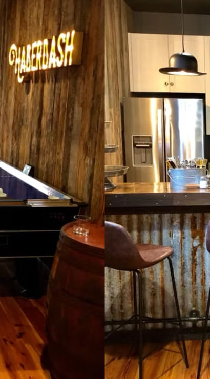 Rustic basement game room featuring an air hockey table and pool table on warm wood floors, an industrial corrugated-metal home bar with leather barstools, pendant lights, stainless fridge and bottles on the counter.