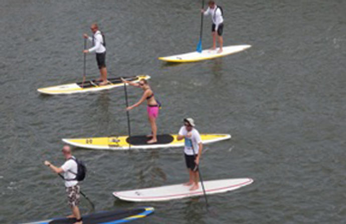Five stand-up paddleboarders gliding on calm water on colorful SUP boards, enjoying outdoor paddleboarding and water-sports recreation.