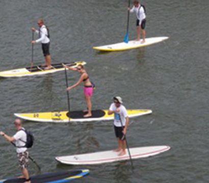 Five stand-up paddleboarders gliding on calm water on colorful SUP boards, enjoying outdoor paddleboarding and water-sports recreation.