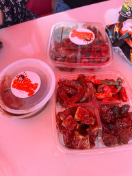 Plastic takeout containers of bright red, tangy chamoy-coated gummies, tamarind cubes and spicy candy pieces with a dipping sauce on a pink table