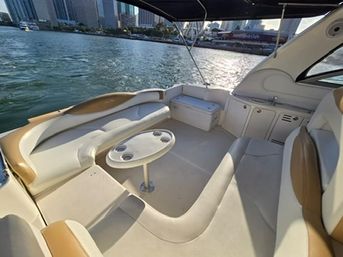 Spacious yacht cockpit with cream-and-tan leather seating and a round table with cup holders, overlooking a downtown waterfront skyline on a sunny day