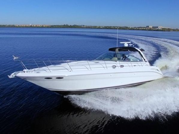 White luxury motor yacht speeding across calm blue water, cutting a curved wake with a faint shoreline on the horizon under a clear blue sky