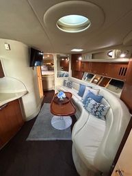 Luxury yacht salon with curved white leather sofa, warm wood cabinetry, oval skylight, wall-mounted TV and a coffee table with blue accent pillows