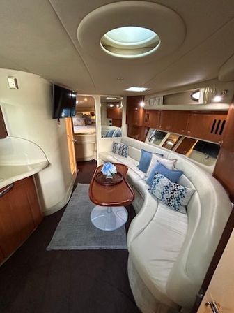 Luxury yacht salon with curved white leather sofa, warm wood cabinetry, oval skylight, wall-mounted TV and a coffee table with blue accent pillows