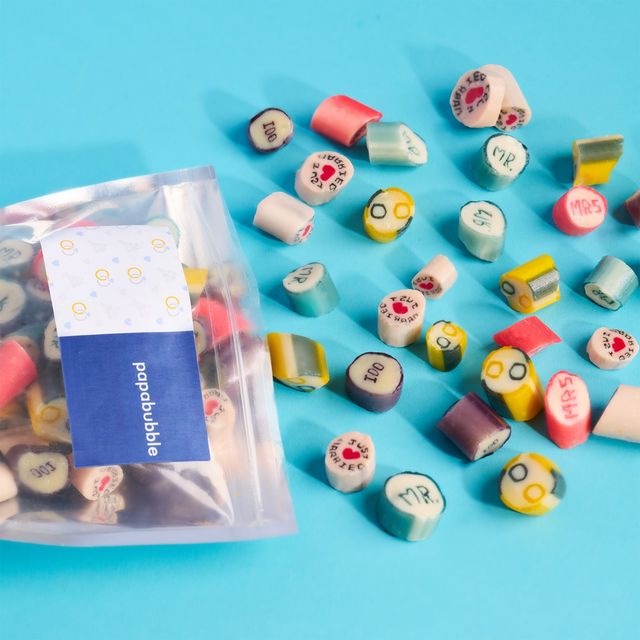 Bright turquoise background with scattered colorful rock-candy slices printed with hearts, 'MR'/'MRS' and "Just Married", and a clear resealable bag at left