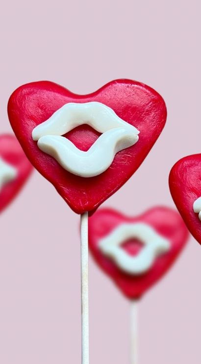 Red heart-shaped lollipops with white candy lips on sticks against a soft pink background, playful Valentine's Day sweets