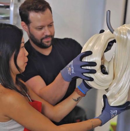 Two people in a candy workshop pull glossy pale taffy off a hook with gloved hands, showcasing artisanal handmade confectionery