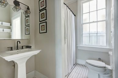 Charming bright bathroom with white pedestal sink, matte black faucet and fixtures, black-and-white hexagon tile floor, white shower curtain and large frosted window.