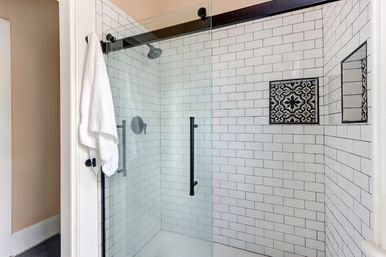 Contemporary bathroom walk-in shower with glass door, white subway tile walls, black matte hardware, patterned tile niche, and a white towel on a hook