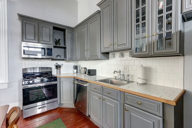 Cozy kitchen with gray cabinets, stainless-steel gas range, microwave and dishwasher, white subway-tile backsplash, tiled countertops with wood trim and hardwood floors.