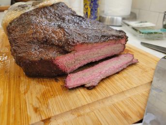 Close-up of smoked beef brisket with dark seasoned bark and pink smoke ring, two juicy slices on a wooden cutting board beside a chef's knife.