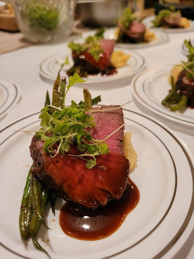Plated gourmet medium-rare beef tenderloin with glossy red wine demi-glace, microgreens, sautéed green beans and piped mashed potatoes on white china at a fine-dining restaurant.