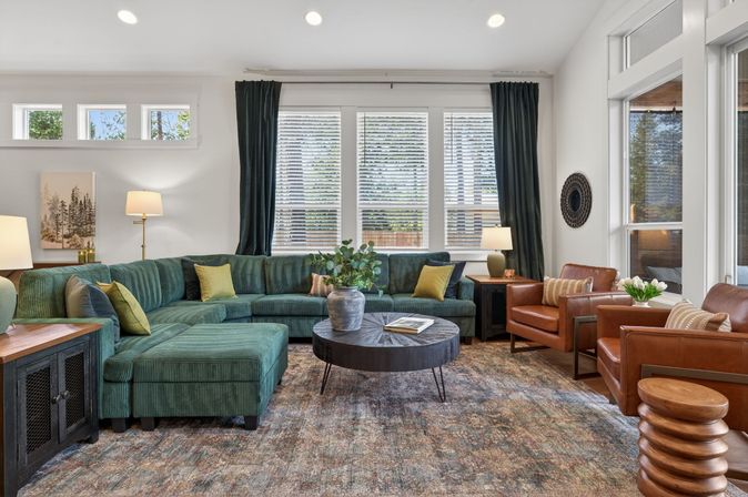 Cozy modern living room with green sectional sofa, cognac leather armchairs, round wood coffee table, textured area rug and large windows