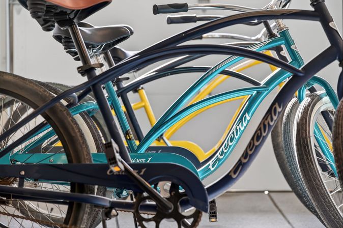 Close-up of vibrant teal and yellow cruiser bicycles lined up in a rack, showing curved frames, seats, pedals and overlapping tires.